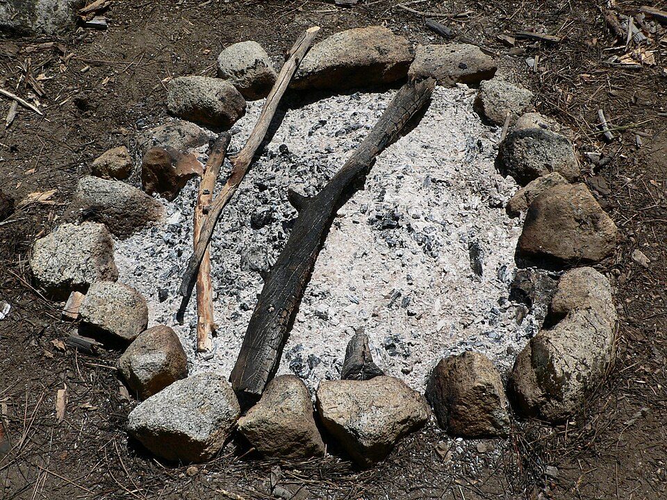 Stone fire ring with ash and charred wood in dirt.